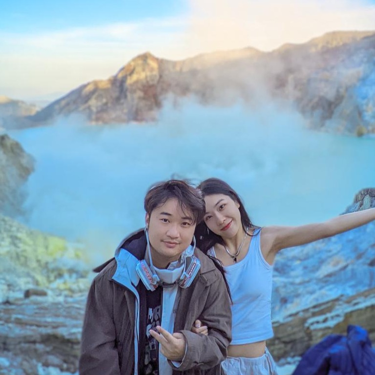 Romantic travel photo of a couple enjoying the breathtaking view of the turquoise Kawah Ijen crater lake at sunrise in Banyuwangi.